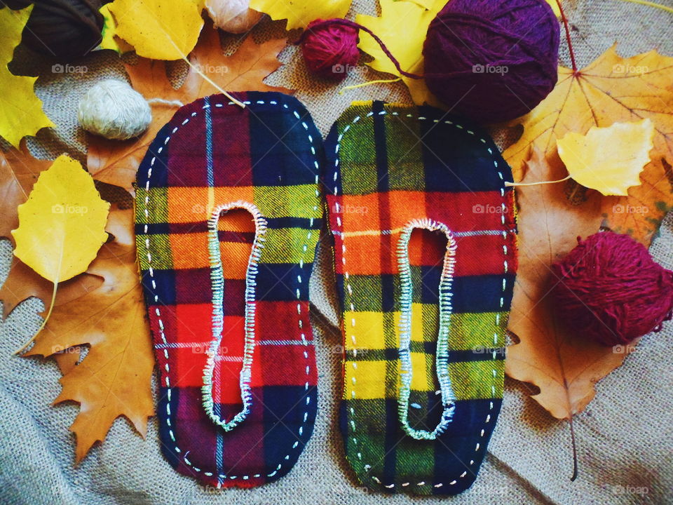 warm homemade slippers with their hands on the background of autumn leaves