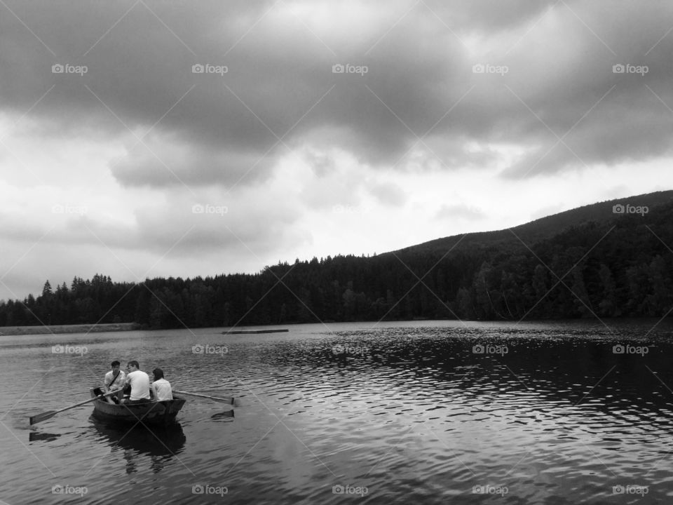 Black and white photograph of boat with people on a lake and storm clouds above