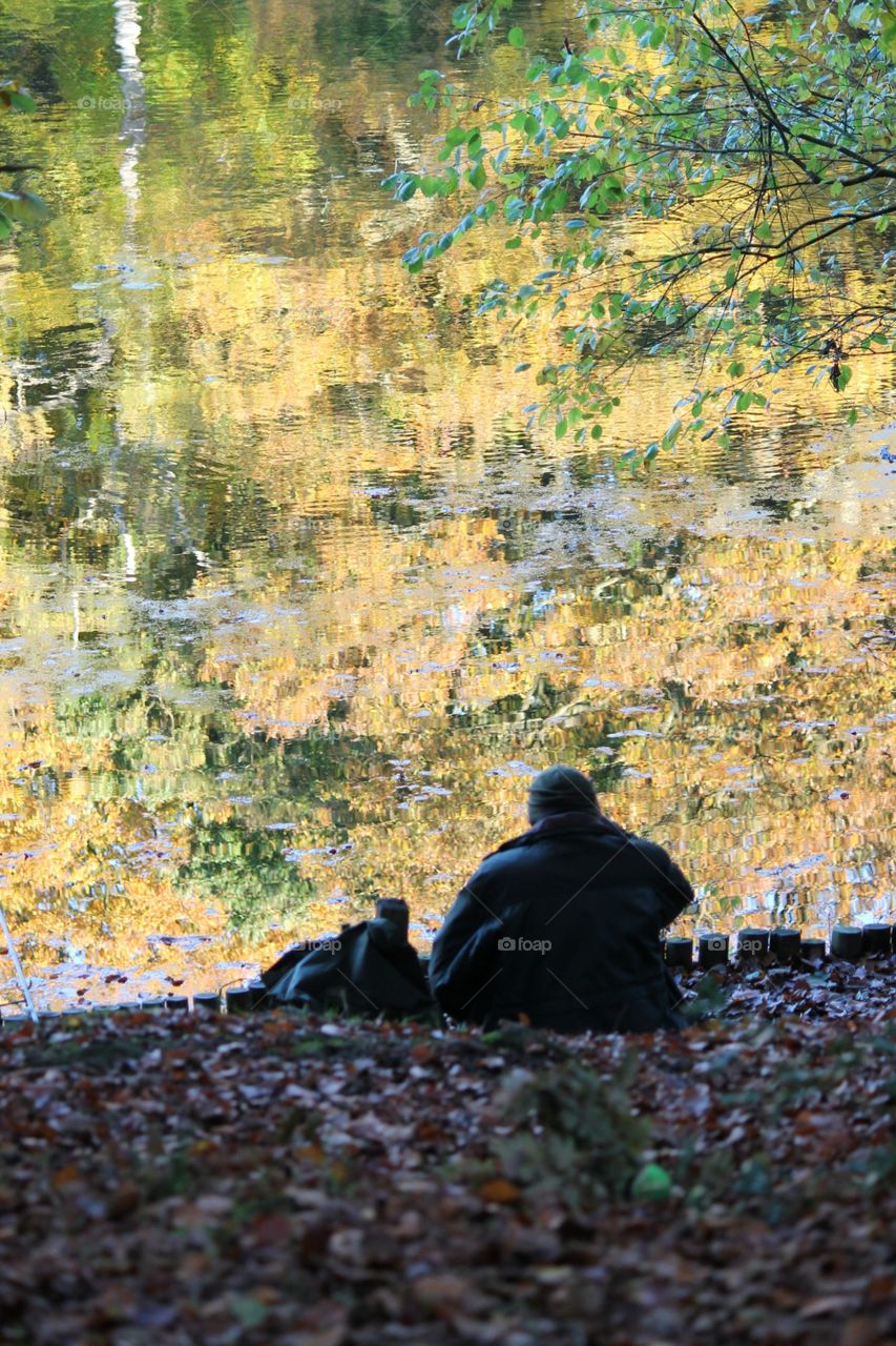Man sits next to lake autumn leaves fall and reflection 