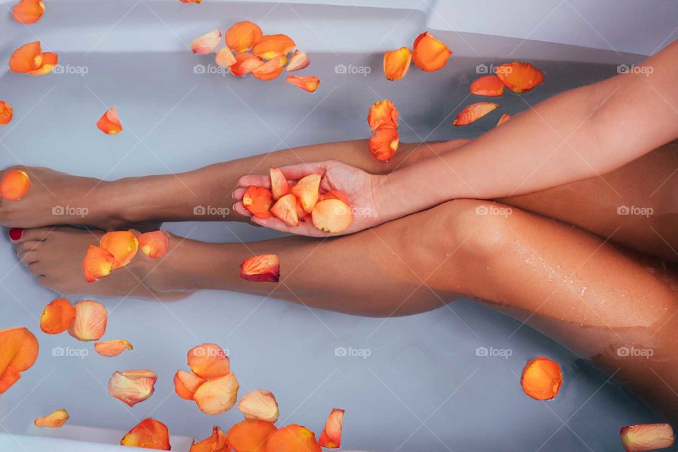 Crop photo of a woman is taking bath with rose petals, legs and hand in the water.