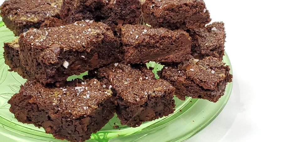 Chocolate brownies on a green glass plate with a white background 