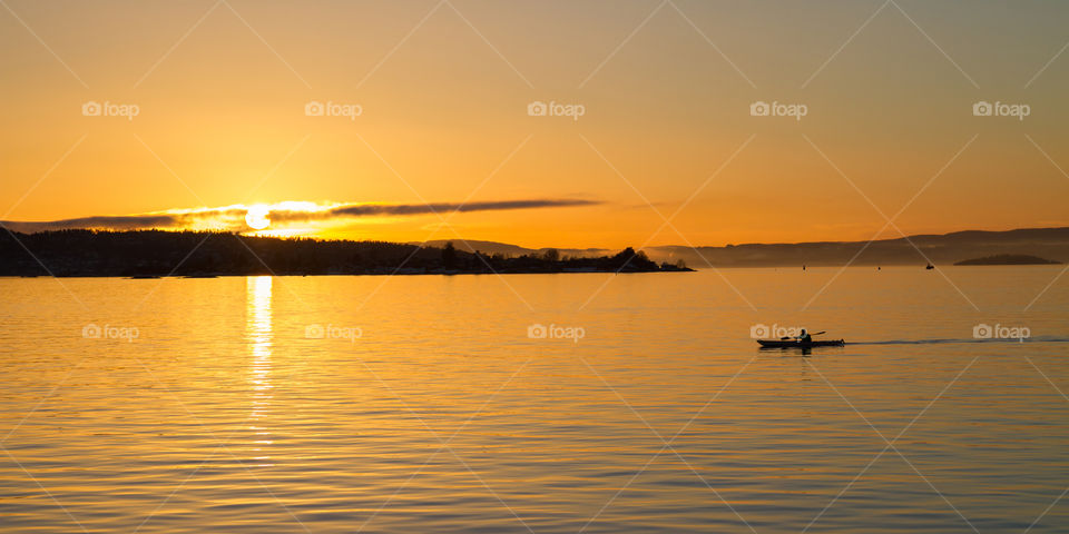 A man in silhouette kayaks across Oslofjord at sunset. 