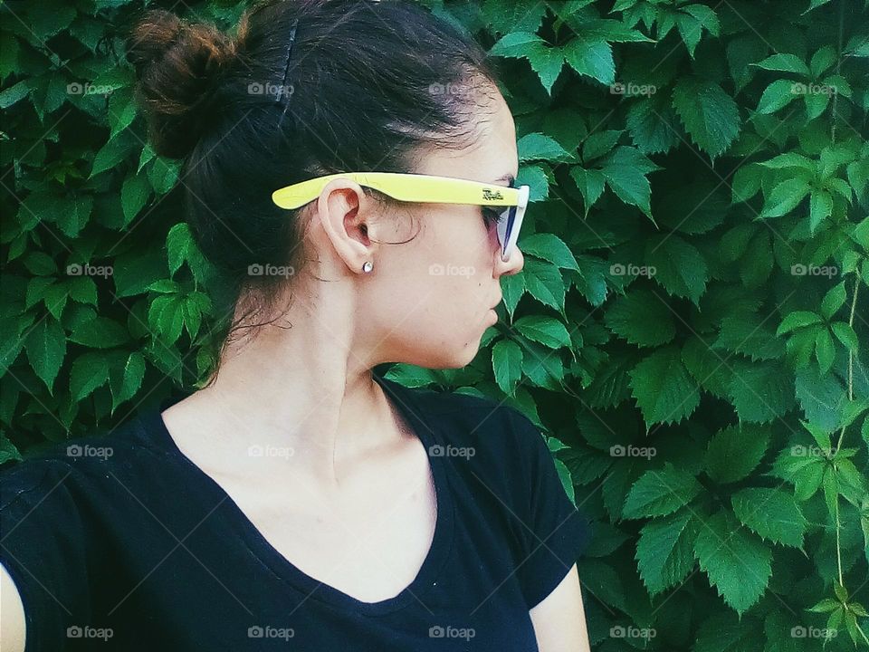 girl in sunglasses on a background of green leaves