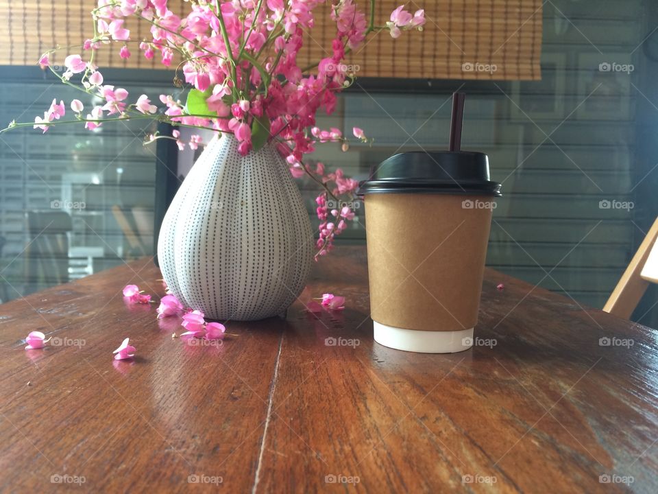 Hot coffee in paper cup with pink flowers in coffee shop