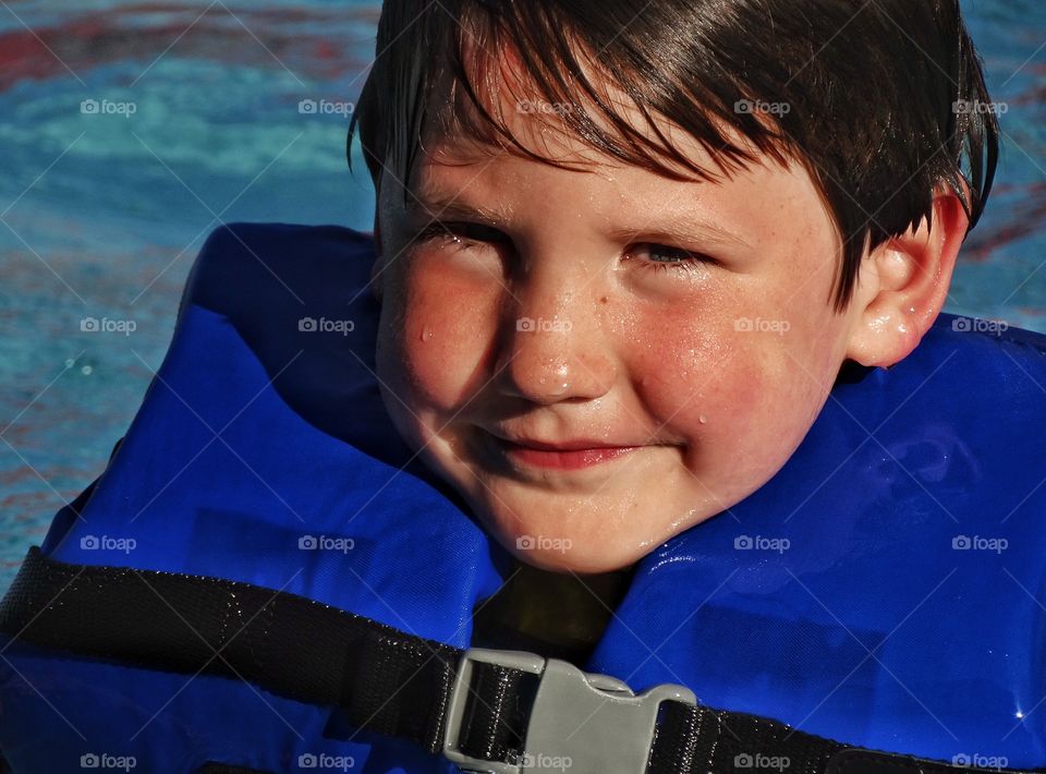 Happy Young Swimmer. Young Boy Wearing A Life Jacket Learning To Swim
