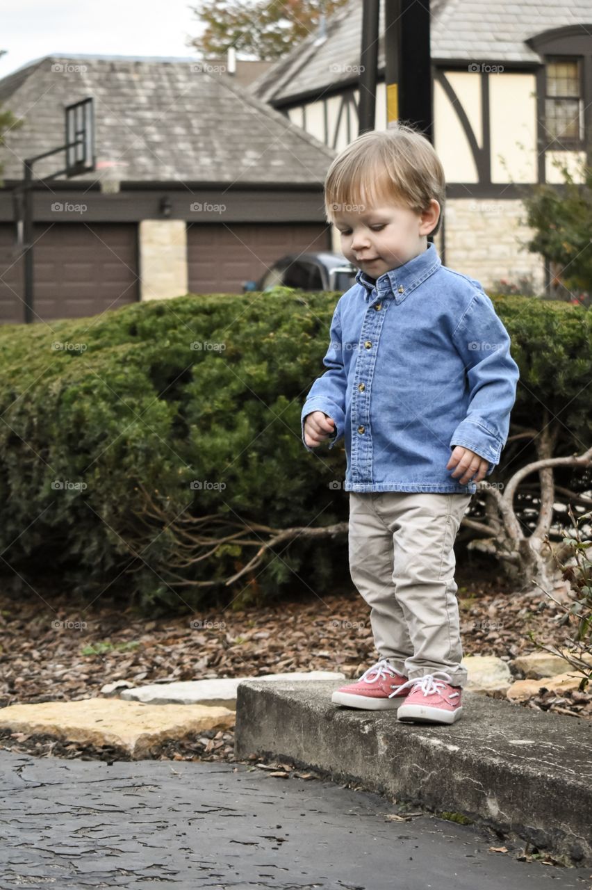 Cute 19 month toddler boy in blue denim shirt playing outdoors 