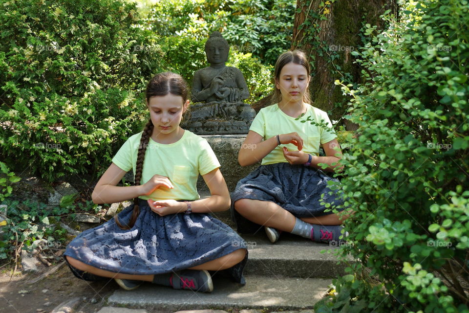 Two girls praying together with a statue of an oriental deity