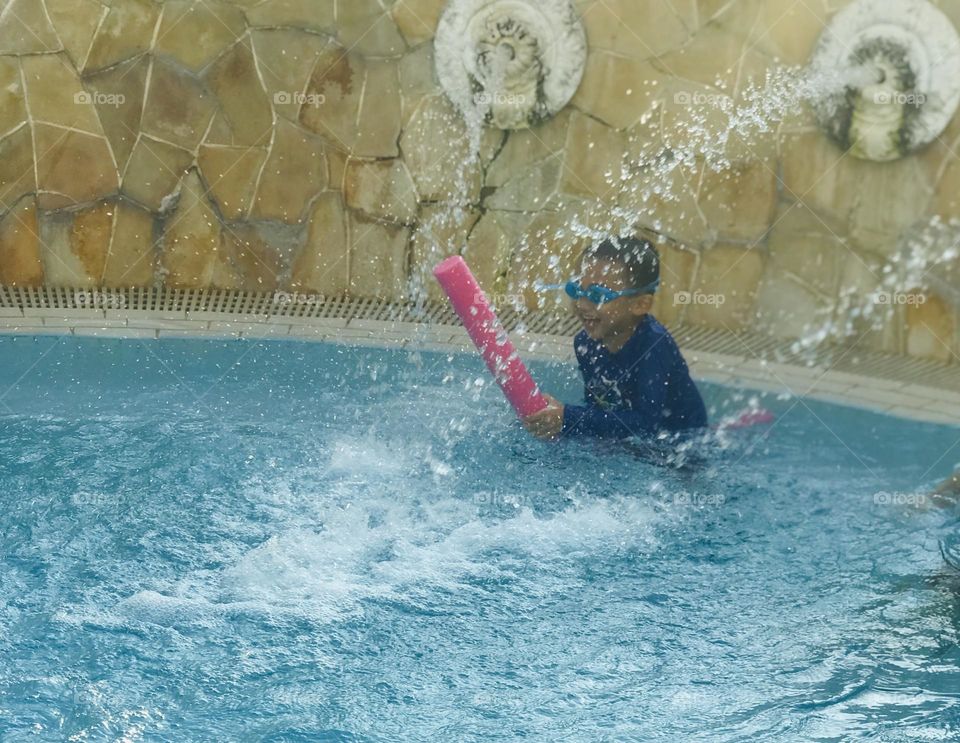 A 6 year old boy enjoying a lot at swimming pool under waterfall in summer 