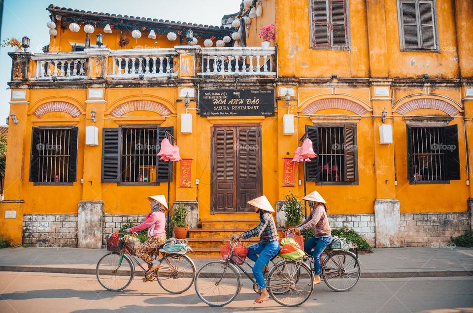 Three women on bikes through Hoi An city