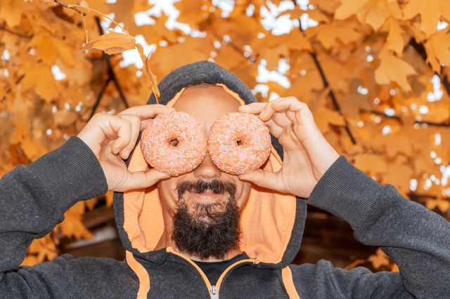 Poryrait of happy man in casual clothes have fun with two doughnuts on autumnal background.