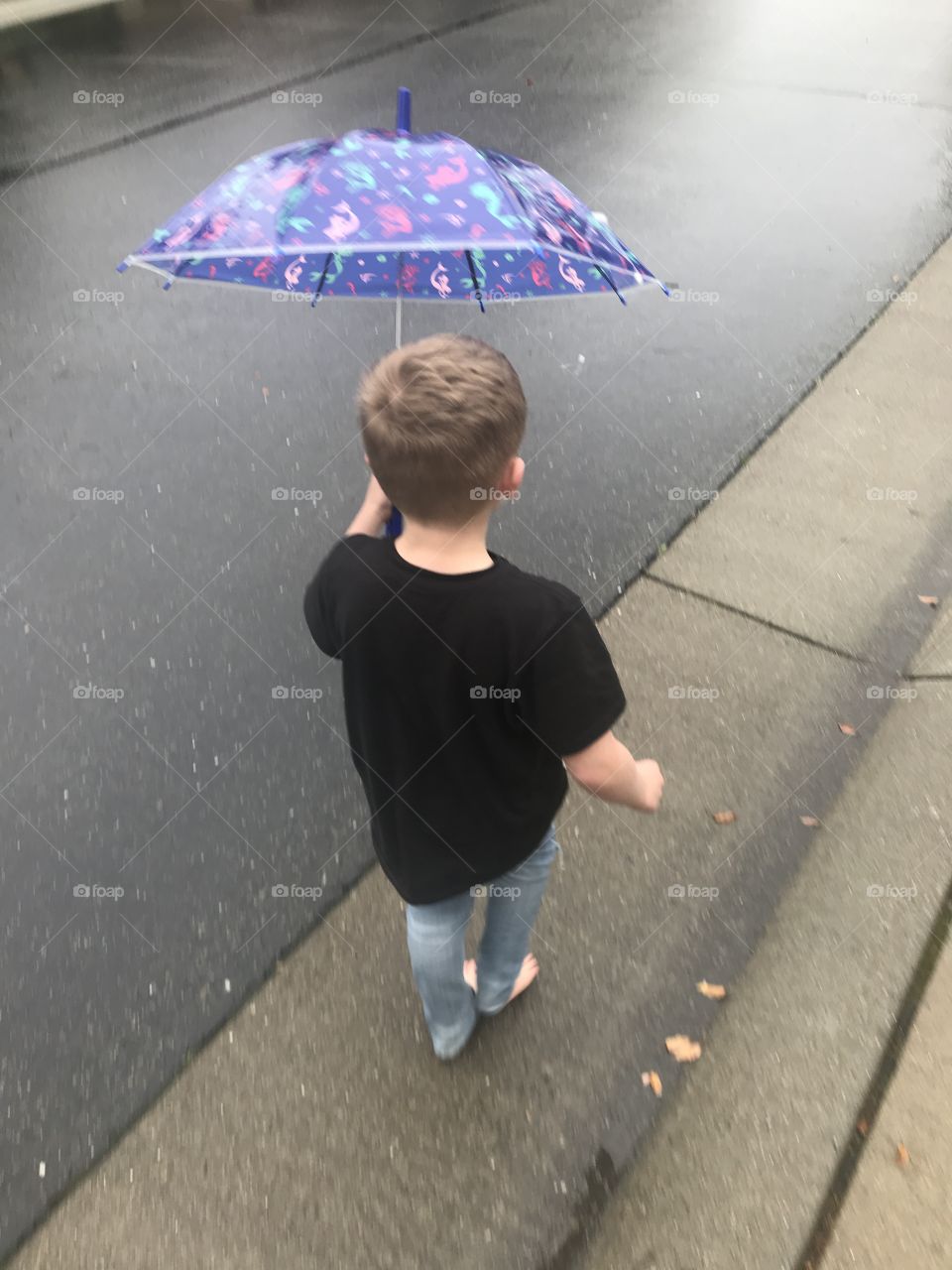 Little boy walking barefoot in the rain with his little umbrella 