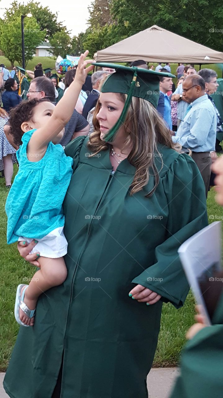 Woman in graduation gown carrying girl
