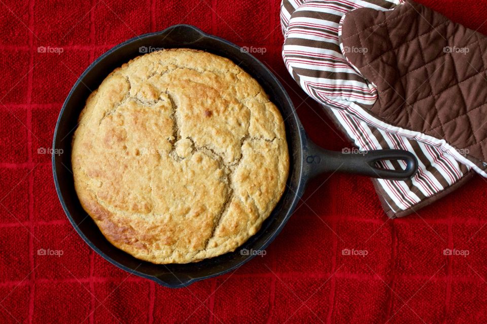 Flat lay of freshly baked sourdough cornbread in a cast iron skillet on a red kitchen towel with red-and-brown-striped oven gripper mitts