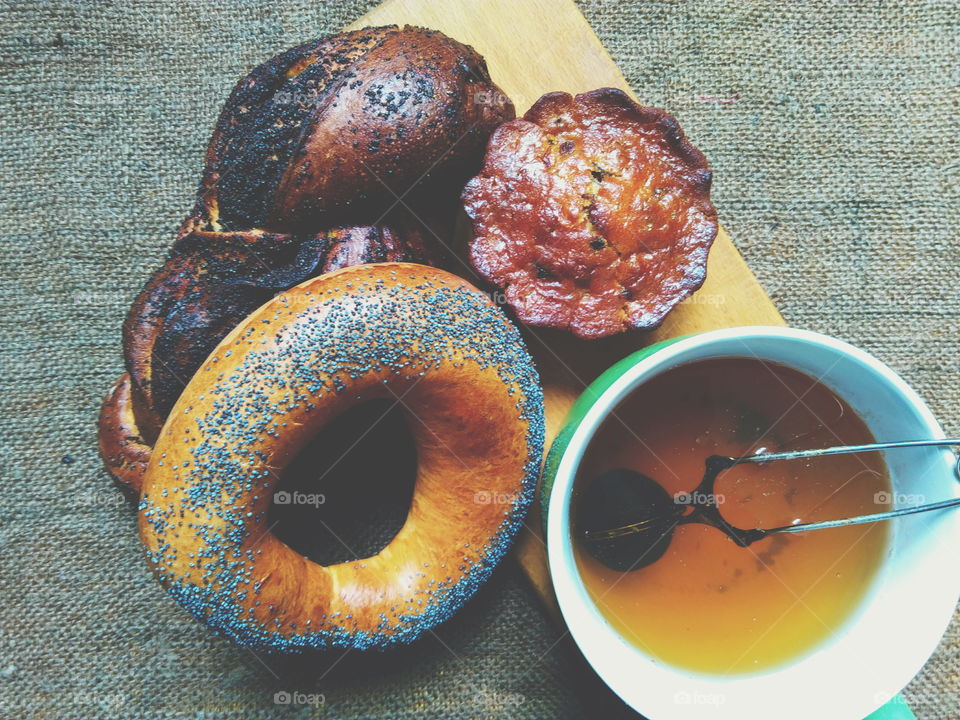 bagel with poppy seeds, basket with poppy seeds, vanilla cupcake and a cup of tea on the table