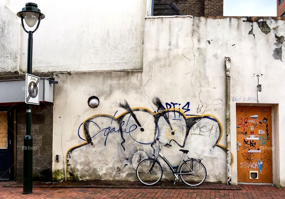 Bicycle leaning against cracked wall with graffiti in street, Hilversum, Netherlands.