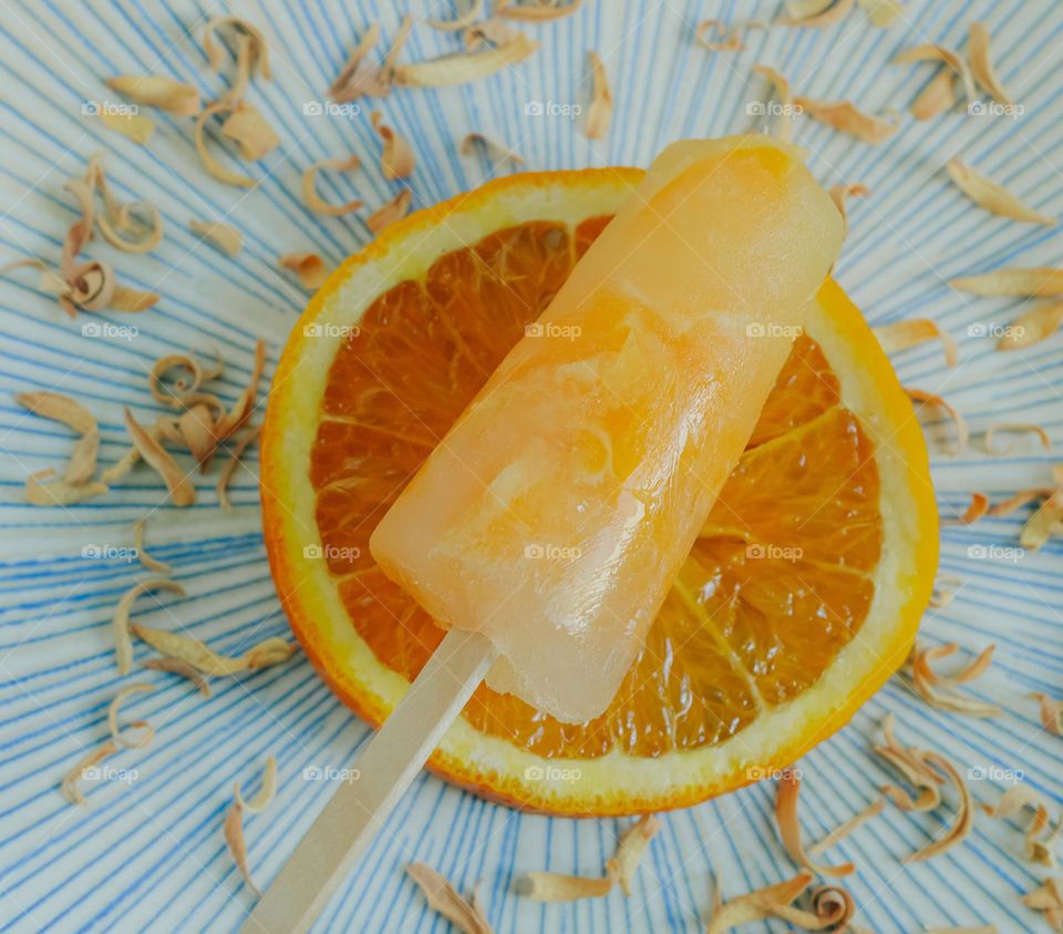 Orange lolly on a large slice of orange, surrounded dried orange peel on a blue patterned plate