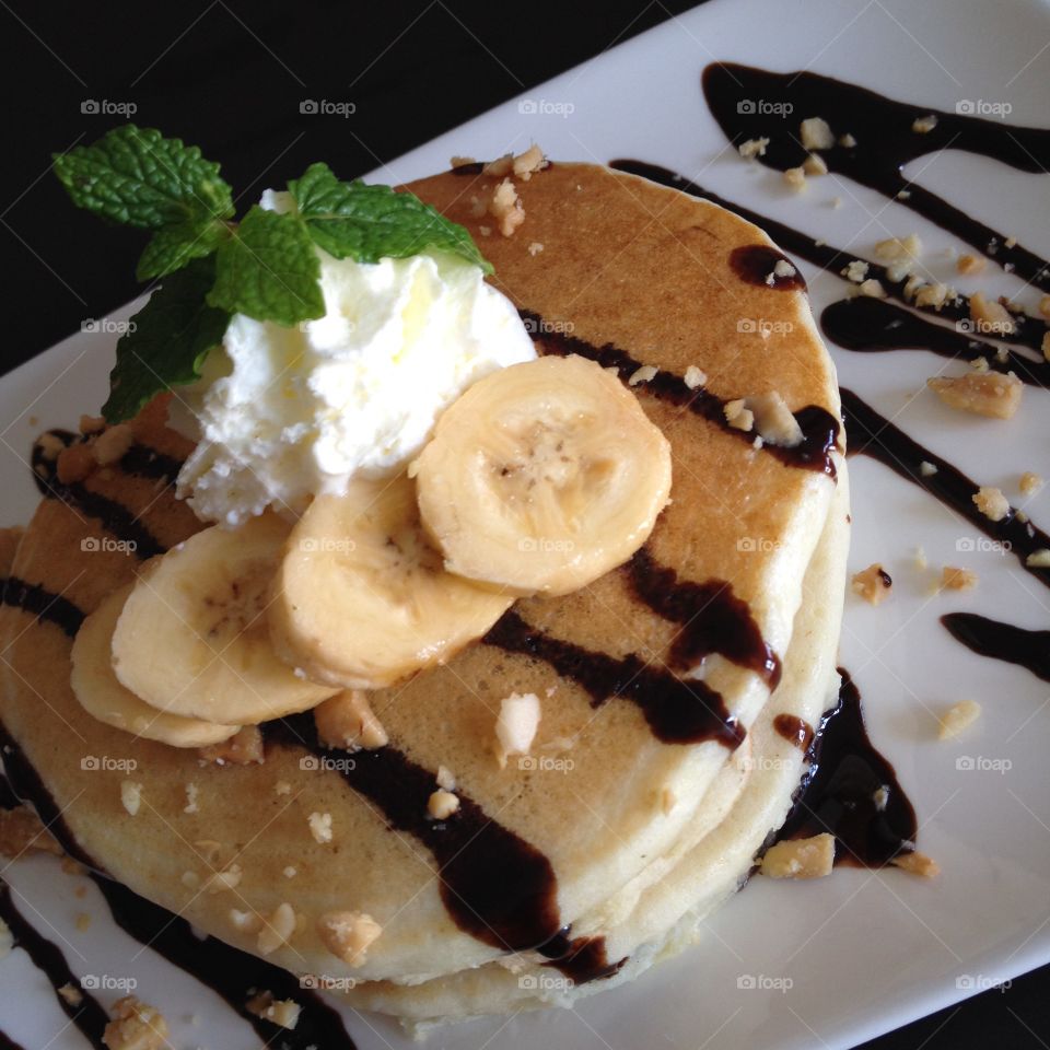 Banana pancakes drizzled in chocolate, topped with whipped cream and nuts.