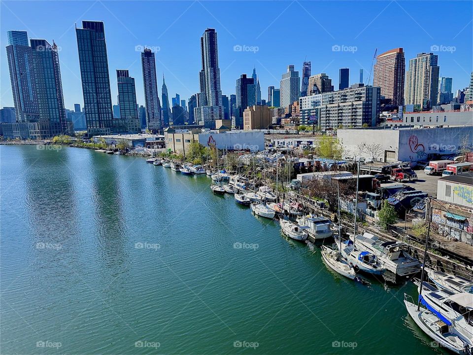 This is “Newtown Creek”, an ocean inlet of the “E River” with its many boats seen from the “Pulaski Bridge” that connects LIC, Queens to “Greenpoint”, Bklyn. In the distance we see “Manhattan” incl. the “Empire State Bldg”. 2024. Hypnotic Productions