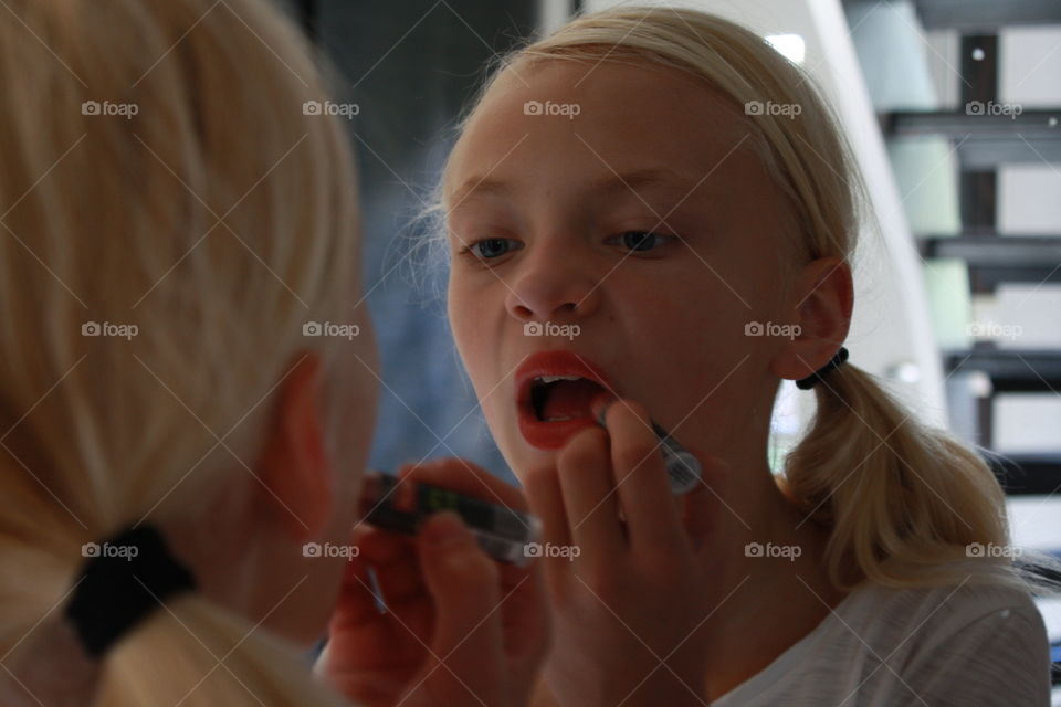 Teenage girl putting on lipstick in front of mirror