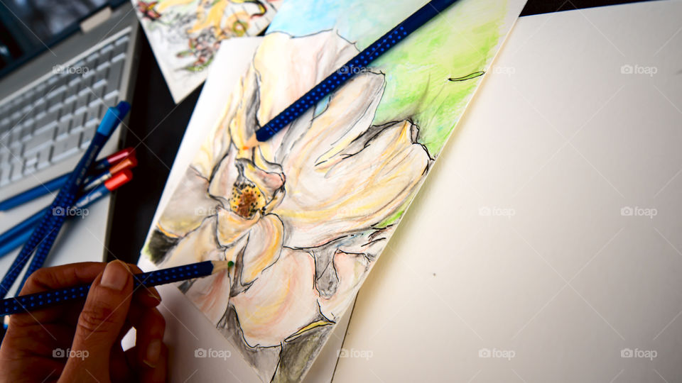 Closeup of hand holding Faber-Castell Art Grip Aquarelle Colored watercolor pencils sketching closeup spring flower with sketchbook on table with laptop and coffee conceptual work life balance, creativity, hobby artist lifestyle photography