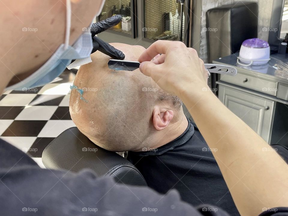 Barber shaving head to the client in the barbershop 