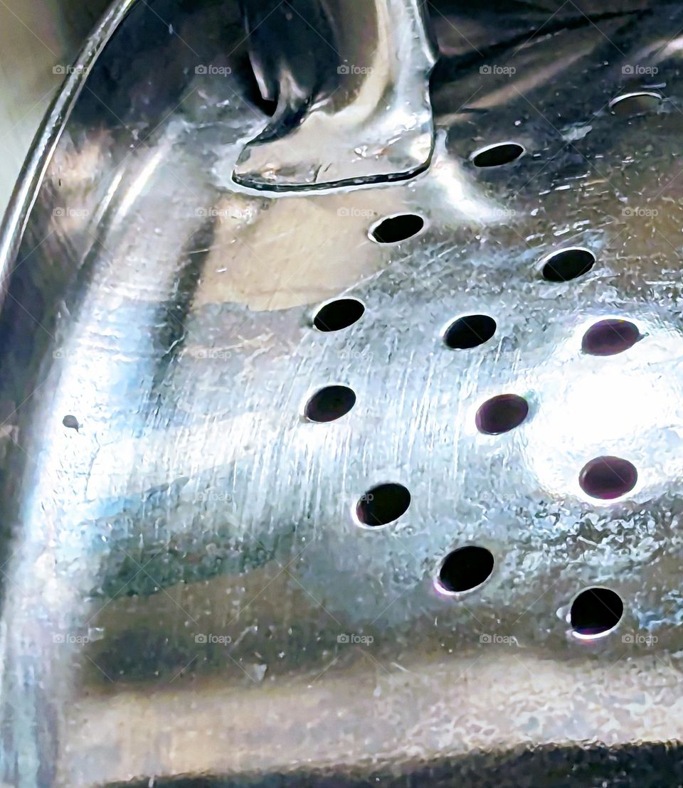 Up close photo showing aging and patina on most used metal kitchen strainer. An essential must have for any kitchen. Love the way the light bounces off the metal and the play of shadows in the back ground.