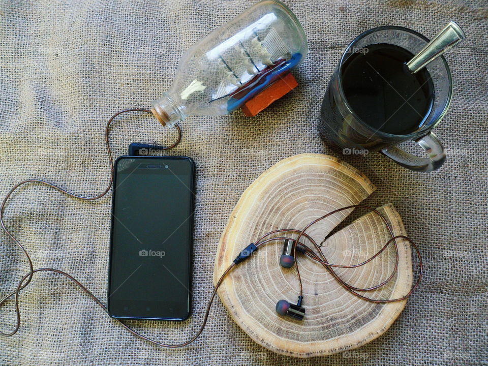 vacuum headphones on a cut-off tree, a smartphone and a cup of black coffee