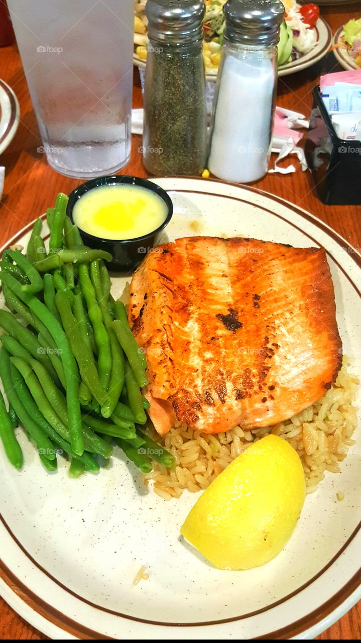 Salmon fillet with rice garnish and green beans with lemon wedge for lunch