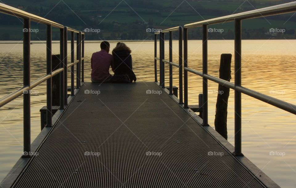 Couple sitting on pier at sunset