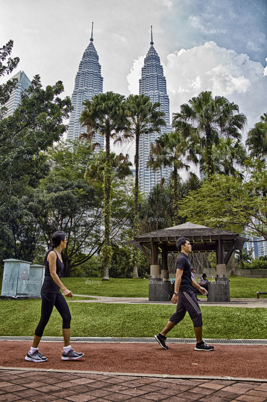 Contrast in the city. people jogging at the park with view of the Petronas twin towers KL