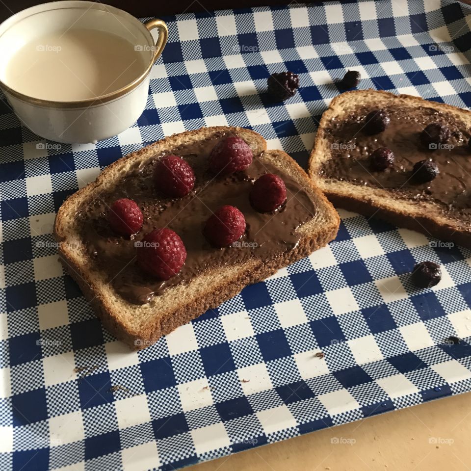 Yummy sandwich slices of wheat bread with Nutella chocolate spread wig raspberries and blackberries and a tea cup displayed on a blue and white serving tray. USA, America