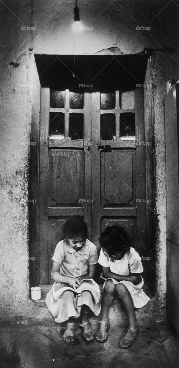 mexico two girls study under a single lightbulb in a poor village in mexico. mexican school girls studying on doorstep. by arizphotog