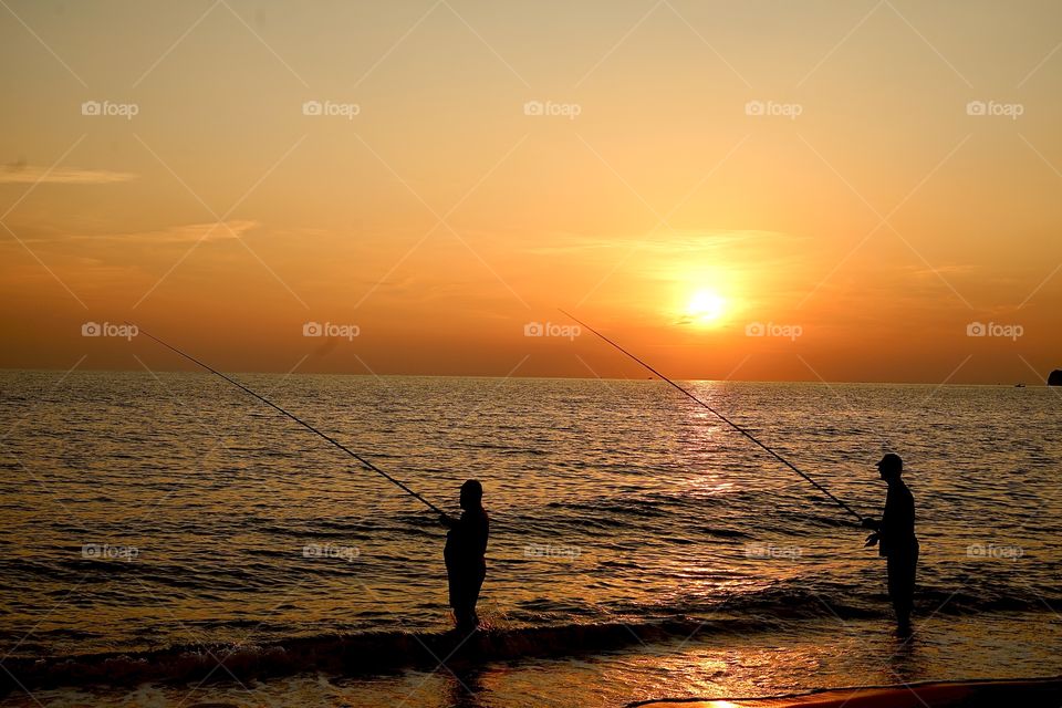 Silhouette of two men fishing beside the beach in sunset time, Alanya, Turkey
