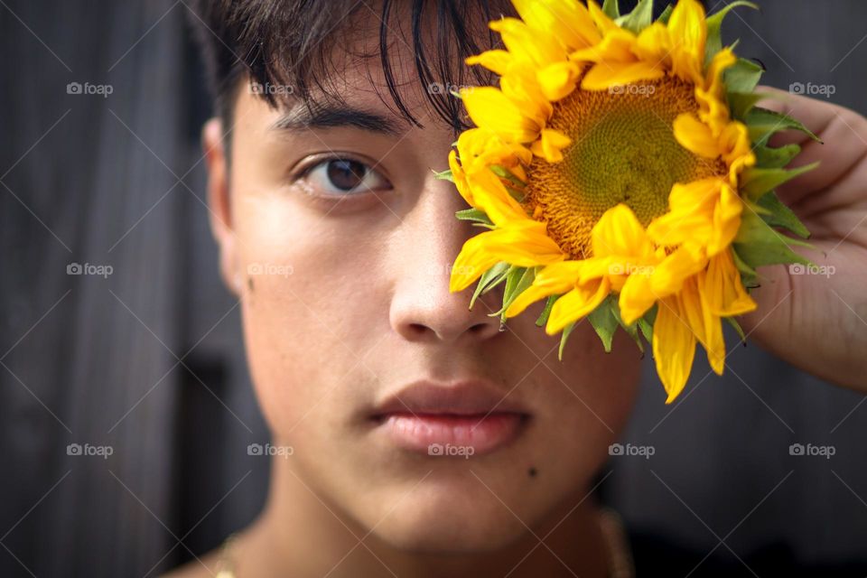 Handsome young man with a sunflower in front of his face