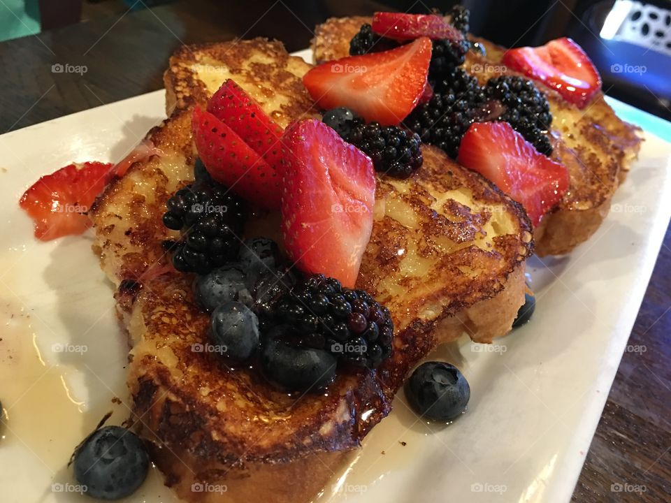 Slices of French toast with a pile of fresh summer berries and maple syrup healthy breakfast with antioxidant rich sliced strawberry, blueberry and blackberry garnish 