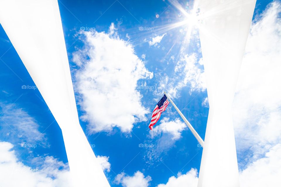 The American flag against the sun, flies over the USS Arizona Memorial at Pearl Harbor Hawaii.  