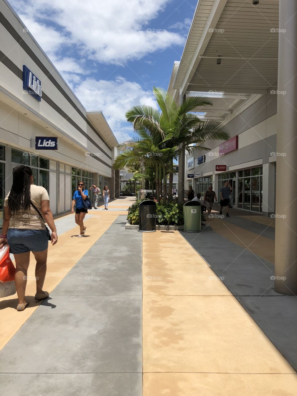 This is an outlet mall in the Daytona beach area in Florida. It was clear skies and sunny that day. Many people were walking around stopping at their favorite shops to try to get a good deal. Featured are the stores Lids and Famous Footwear.