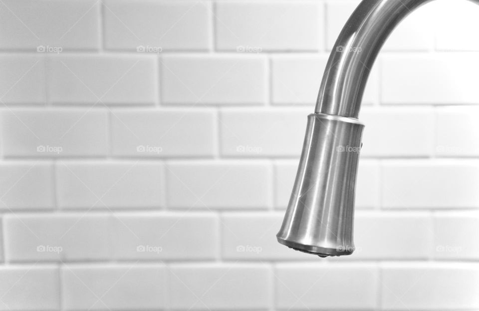 Stainless steel kitchen tap faucet foreground, isolated on blurred white subway tiled wall, conceptual home, elements, design, function, cleaning, food preparation, background backdrop image with plenty of text copy space 