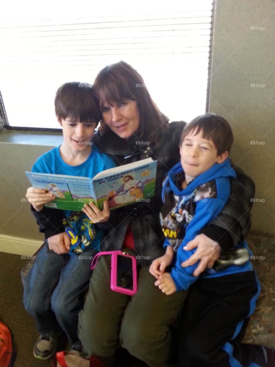 A grandma reading to her two grandsons, keeping them entertained in dr waiting room. 