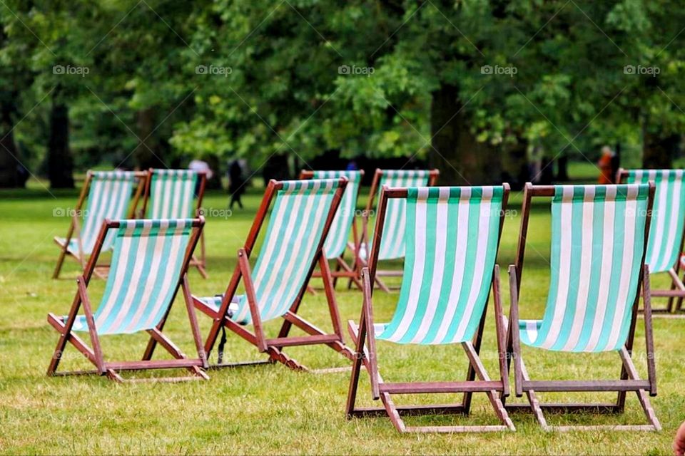 Empty white green striped lounge chairs stand on a lawn in a city park