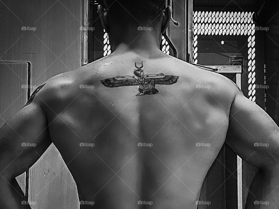 Back of a man with a tattoo of the ancient Egyptian Goddess Aset or Eset, who is commonly known today by her Greek name Isis. Aset had great powers of healing, protection, and magic; her power transcended that of all other deities.