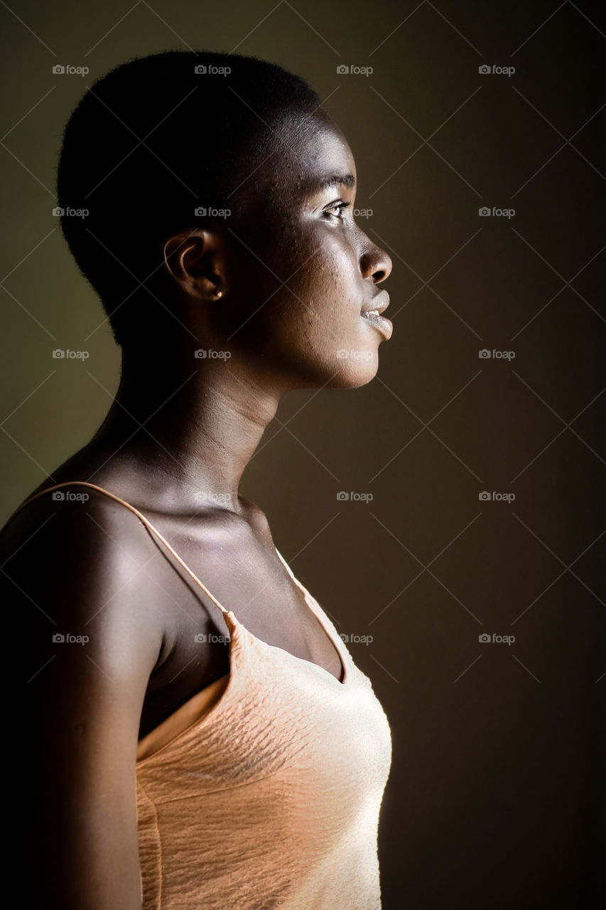 Beautiful african teenage girl smiling and staring upwards in a partial dark room.