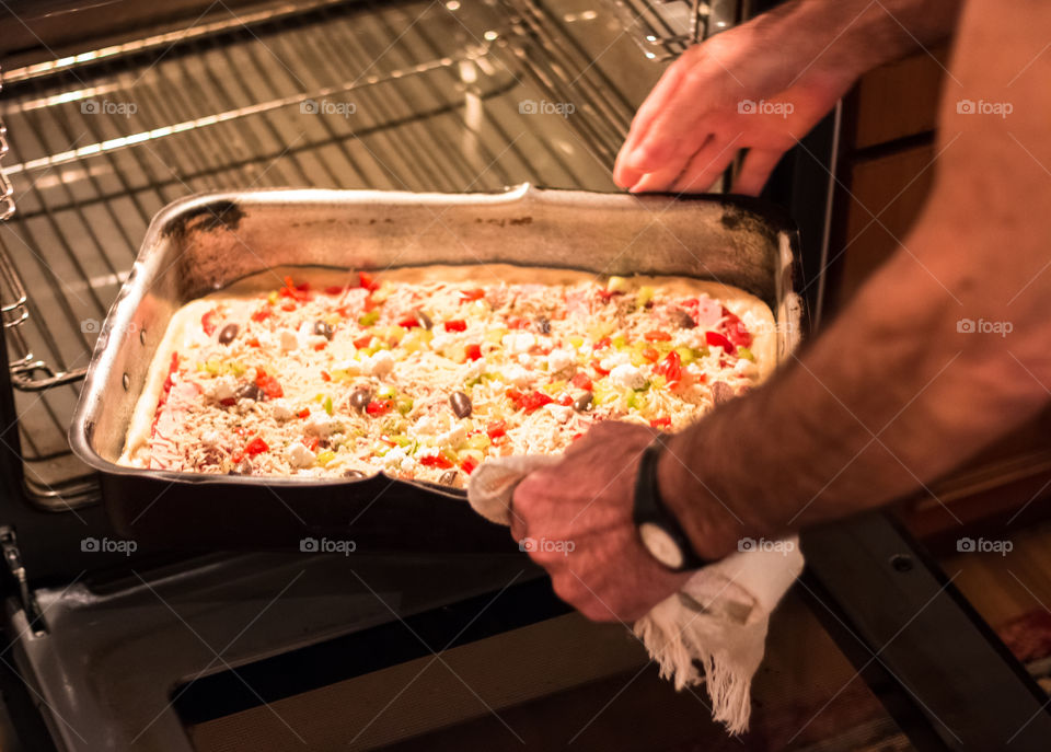 Man Putting Home Made Pizza In The Oven For Baking
