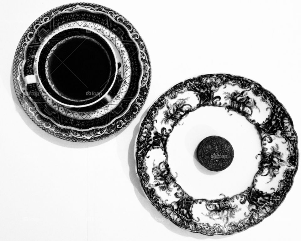 Black and white photo of tea/coffee cup and saucer and biscuit on vintage porcelain plate