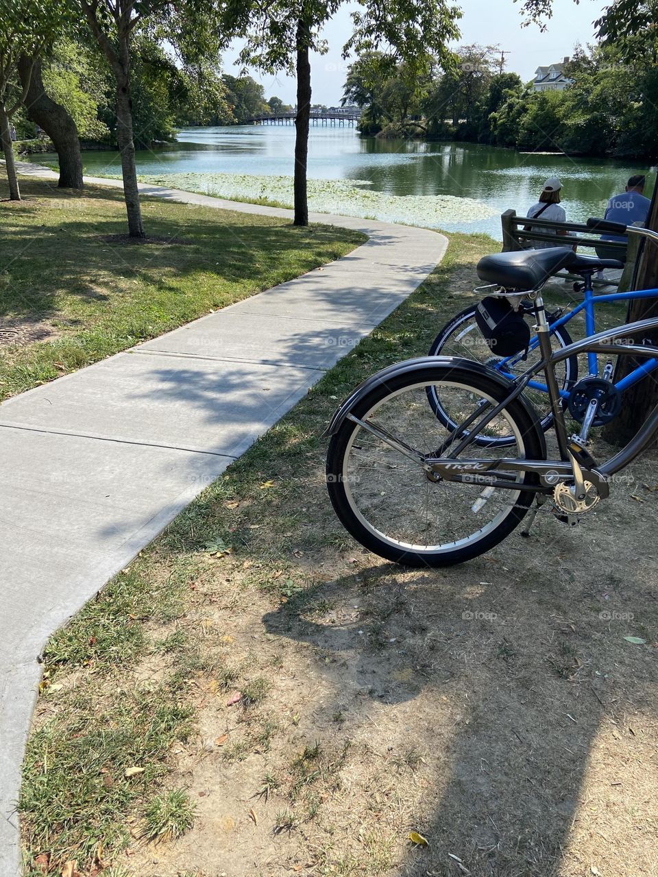 A couple sits on a bench facing the lake in Divine Park in Spring Lake, NJ with their bikes parked behind them. The park is very tranquil and is a good place to ride - and rest.