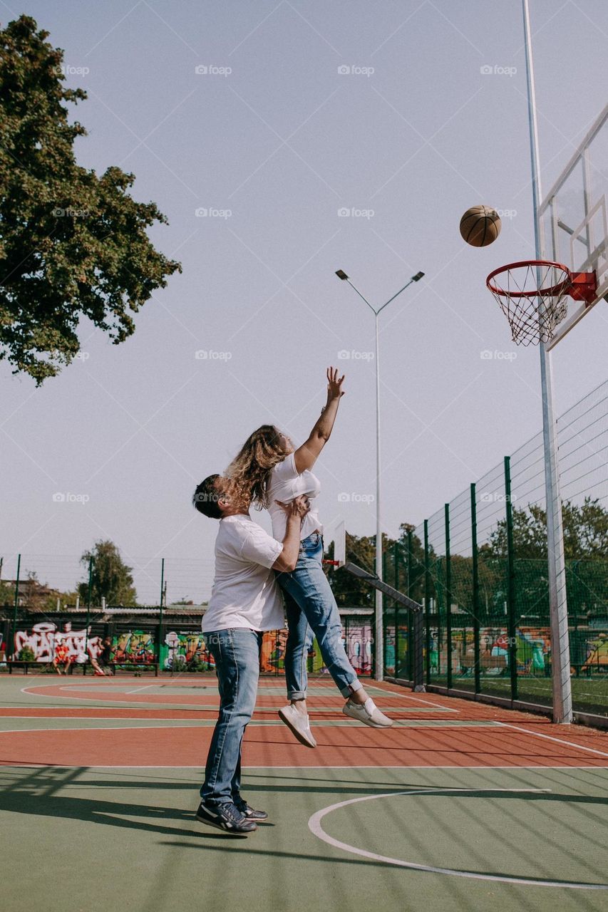 Boy and girl playing basketball. Boy help and holding girl