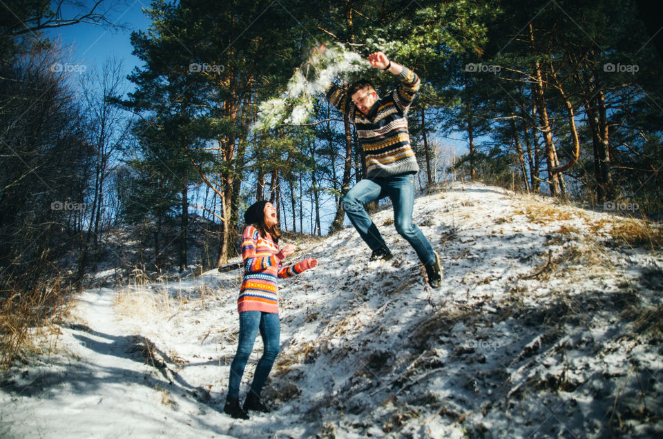 Young man jumps from a hill and throws the snow from the branch of tree on his girlfriend. Winter activity lifestyle concept
