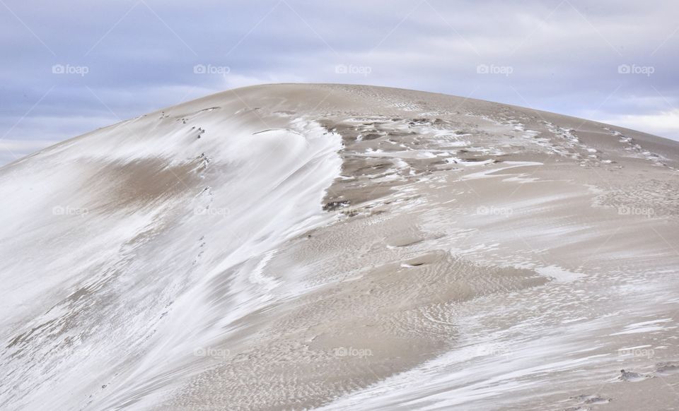 Great Sand Dunes National Park covered in snow. Very cloudy and moody shot with deep lighting. One dune is the focal point.