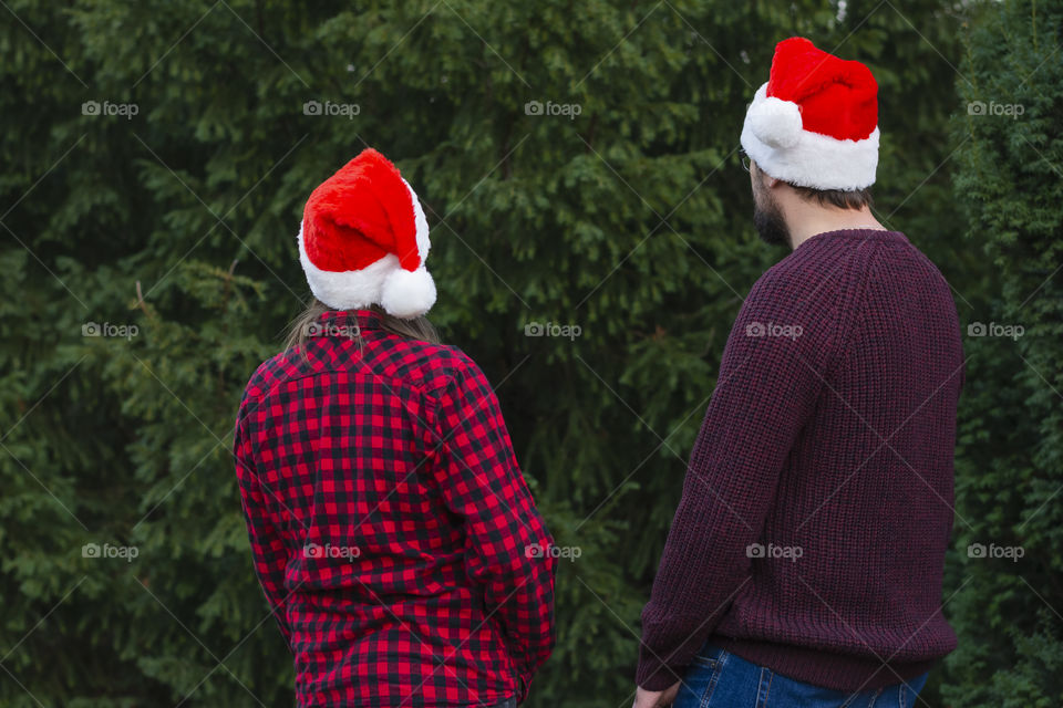 Back view young couple in Santa hats celebration Merry Christmas outdoors Christmas tree outdoors. Concept: winter holidays weekend merry christmas Black Friday