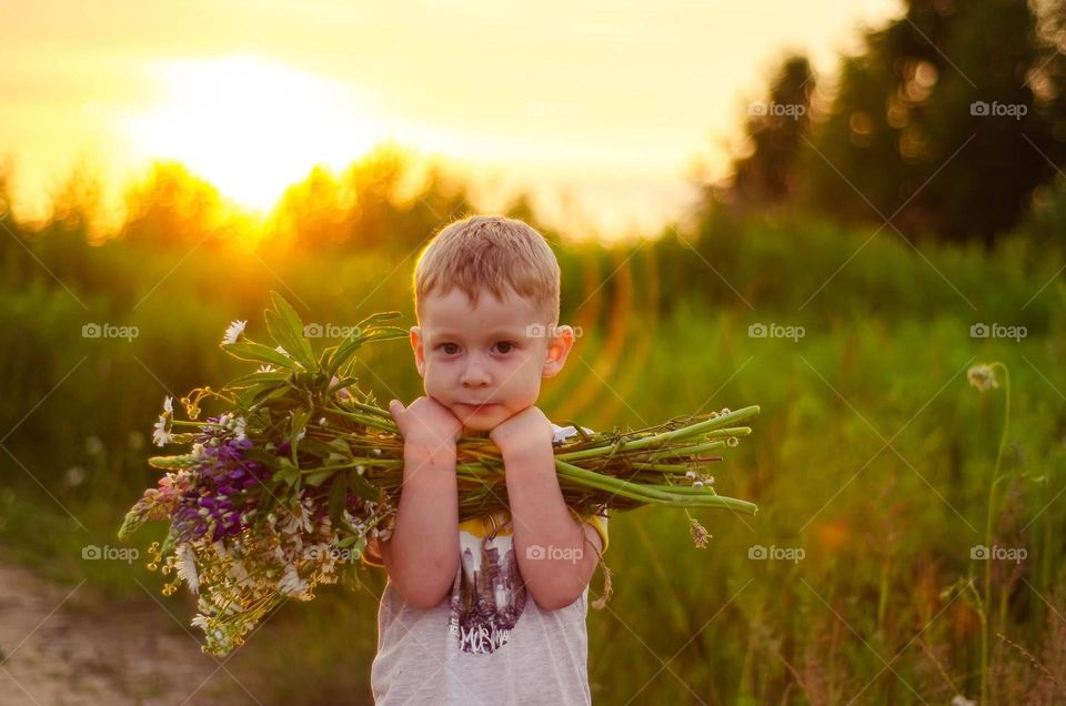Boy with a big bouquet of flowers in the sunset rays.